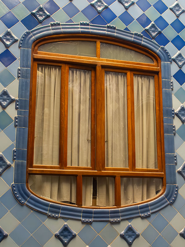Unusual shaped inside wooden window with curtains inside Gaudi designed house in Barcelona