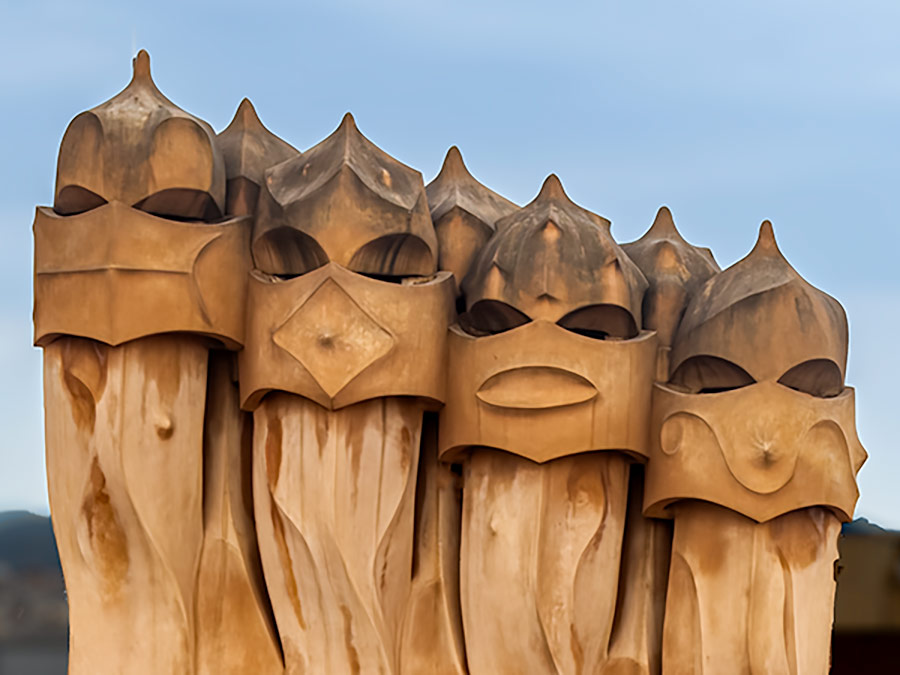 Unusual shaped columnar, wooden sculptures with faces on roof of Gaudi designed house in Barcelona.