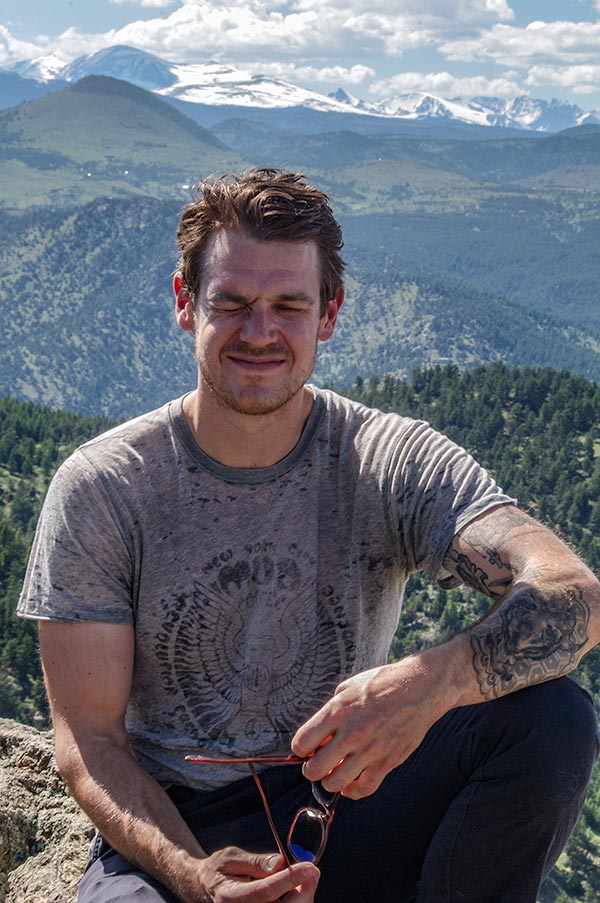 Man half-smiling with sun in eyes and mountains in background